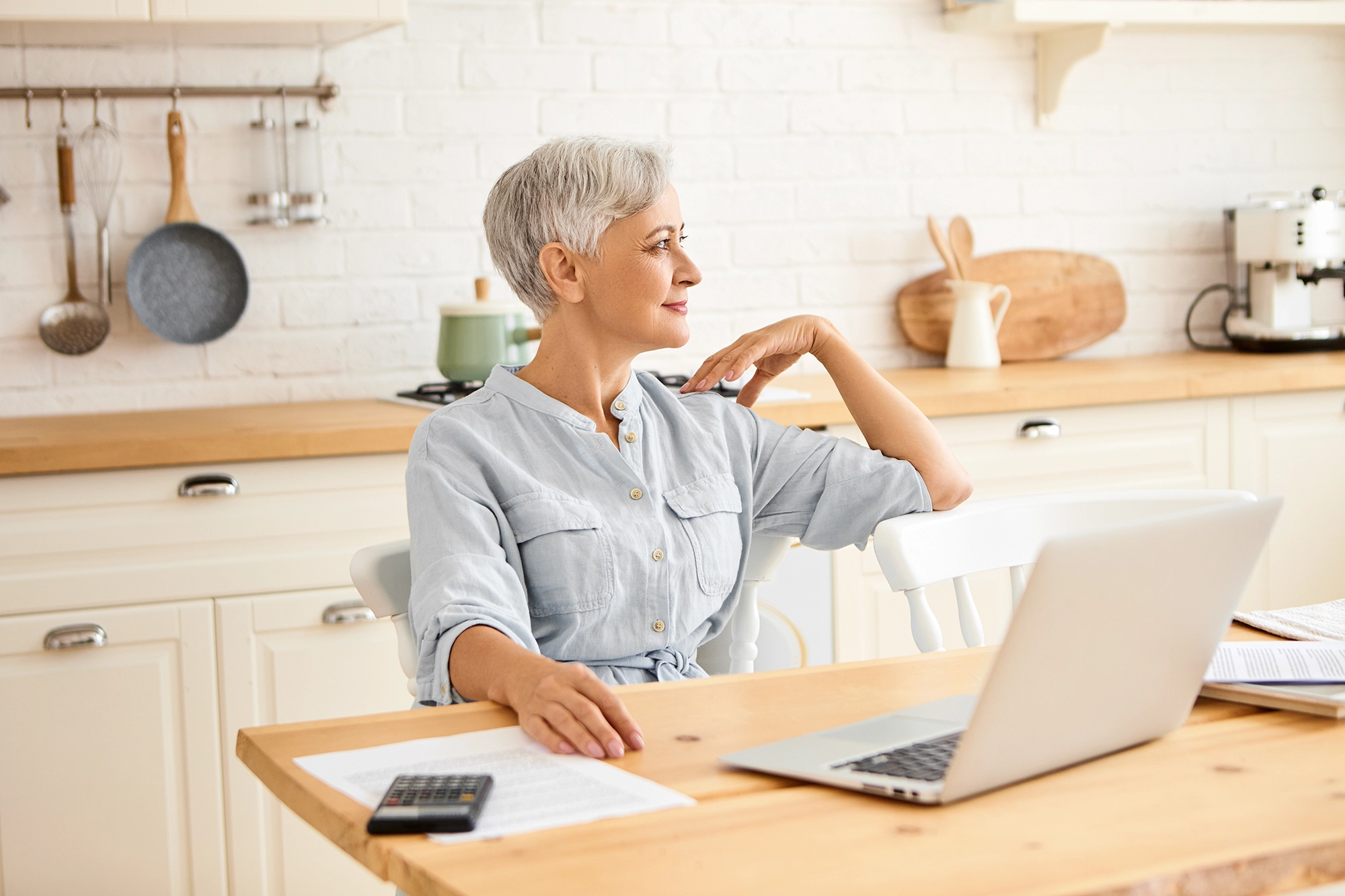 A mature person at a kitchen table with sunlight, a glass of water, and a notebook to plan the day