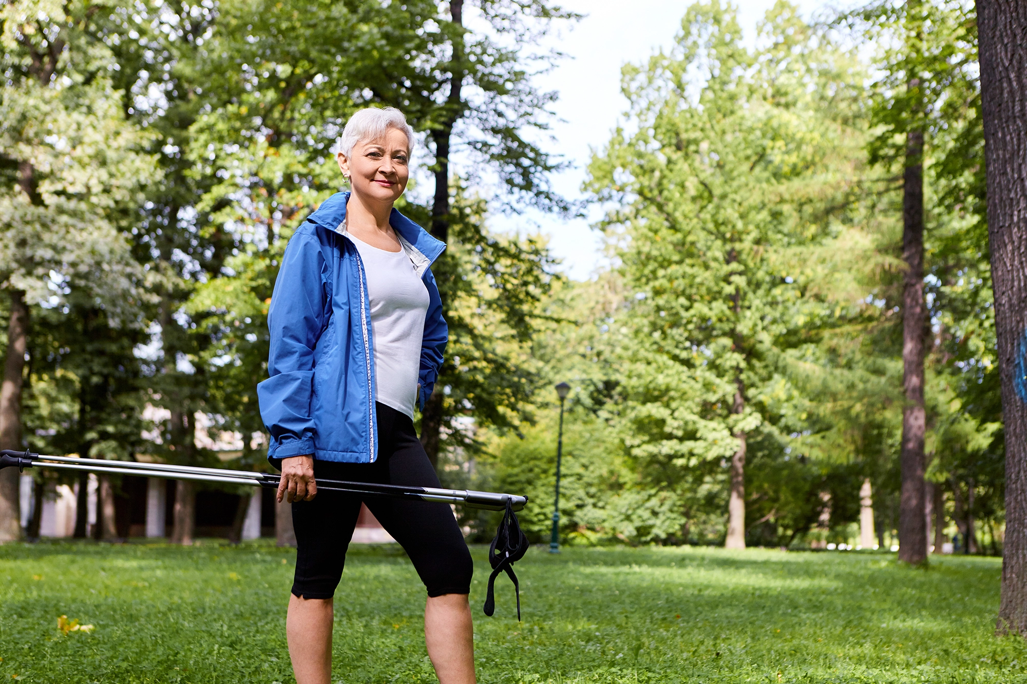 A smiling mature woman standing in a sunlit park, feeling hopeful and confident